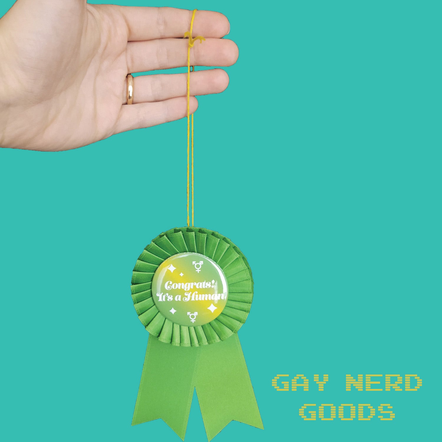 hand holding up the thread of the "congrats it's a human" award ribbon on a mint green background