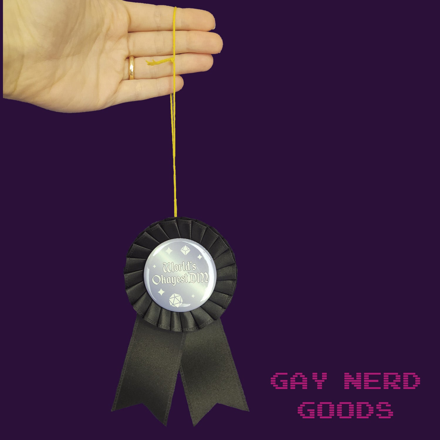 hand holding the thread loop of the black world's okayest DM award ribbon on a purple background