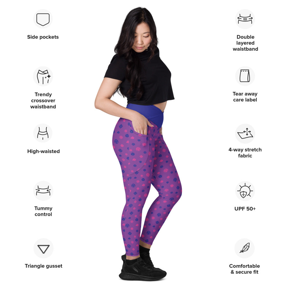 Light-skinned dark-haired female-presenting model wearing the bisexual dice leggings. she is facing right and has a hand in the pocket. she is surrounded by product specs: "side pockets, trendy crossover waistband, high-waisted, tummy control, triangle gusset, double layered waistband, tear away care label, 4-way stretch fabric, UPF 50+, comfortable & secure fit"