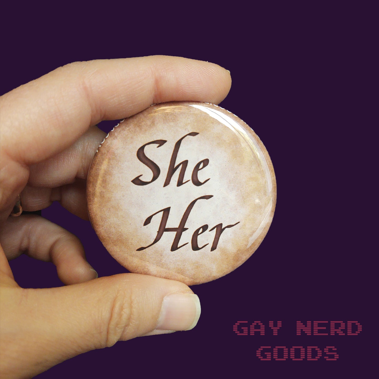 she her large calligraphy pronoun button held in two fingers on a dark purple background