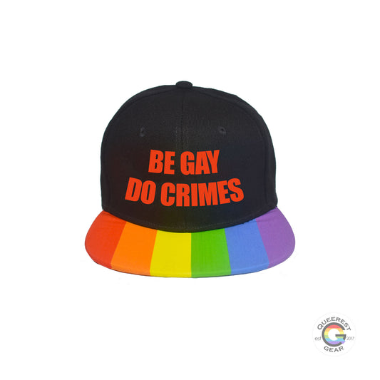 Custom black flat bill snapback hat. The brim has the rainbow pride flag on both sides and the front of the hat has the phrase "be gay do crimes" in red. Front view