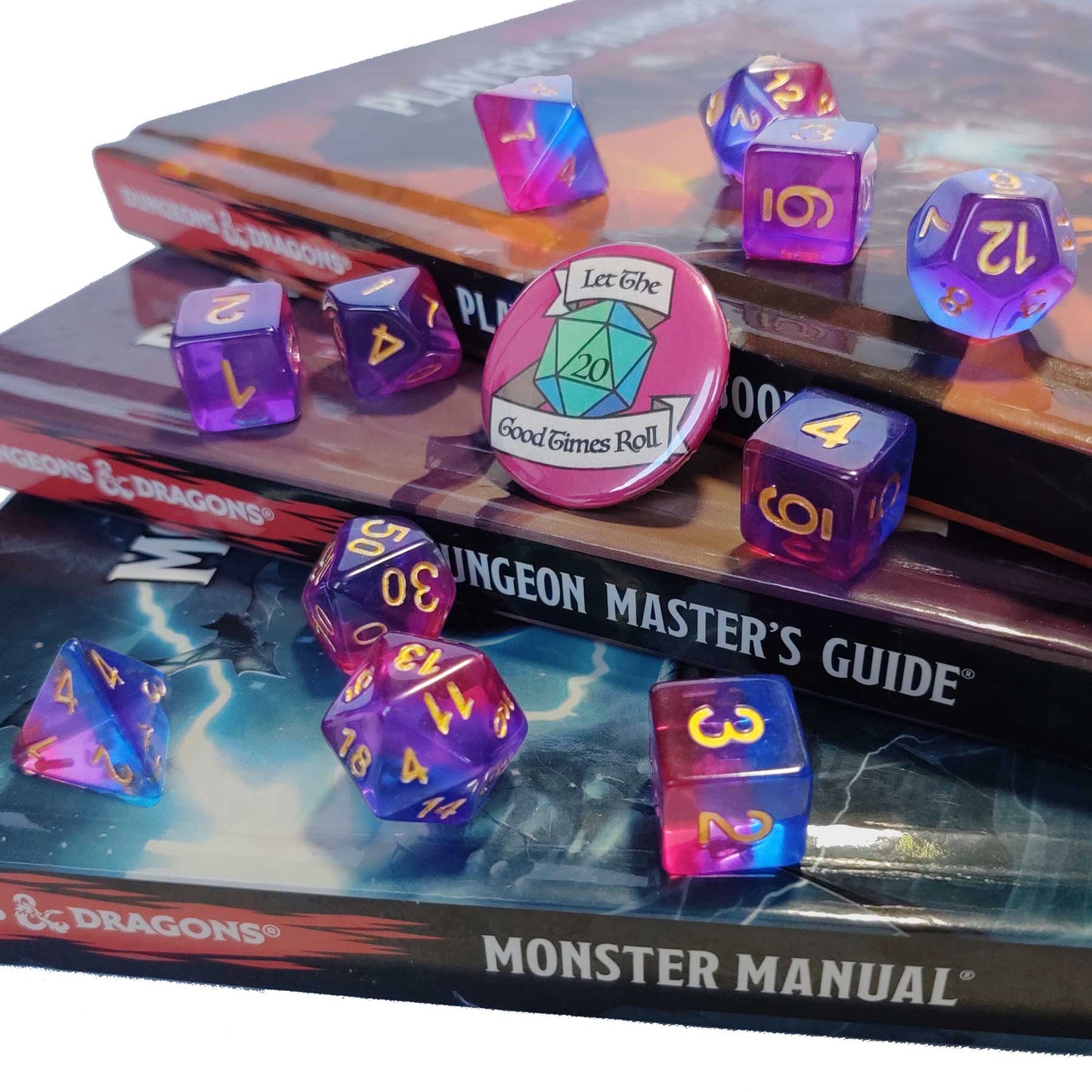 11 piece set of polyhedral dice scattered on a stack of D&D books. They are transparent and colored in the stripes of the bisexual flag with gold ink. There is the freebie “let the good times roll” pinback button among them. 