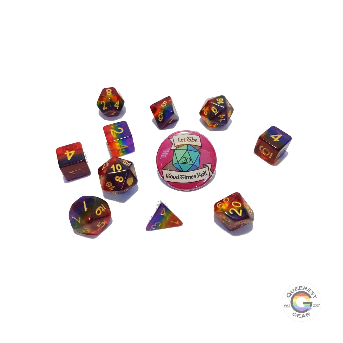 11 piece set of polyhedral dice scattered on a white background. They are transparent and colored in the stripes of the rainbow flag with gold ink. There is the freebie “let the good times roll” pinback button among them. 