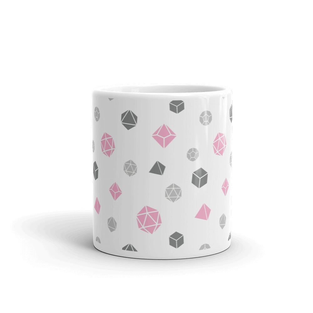 white mug on a white background with handle facing back. It has an all-over print of polyhedral d&d dice in the demigirl colors of dark grey, light grey, pink