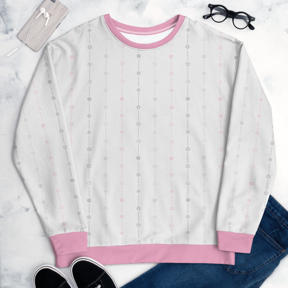 The demigirl pride sweater laying flat, surrounded by clothes, a phone, and glasses. the sweater is white and has stripes of dashed lines and polyhedral dnd dice in greys and pink. The cuffs, collar, and waistband are a matching pink