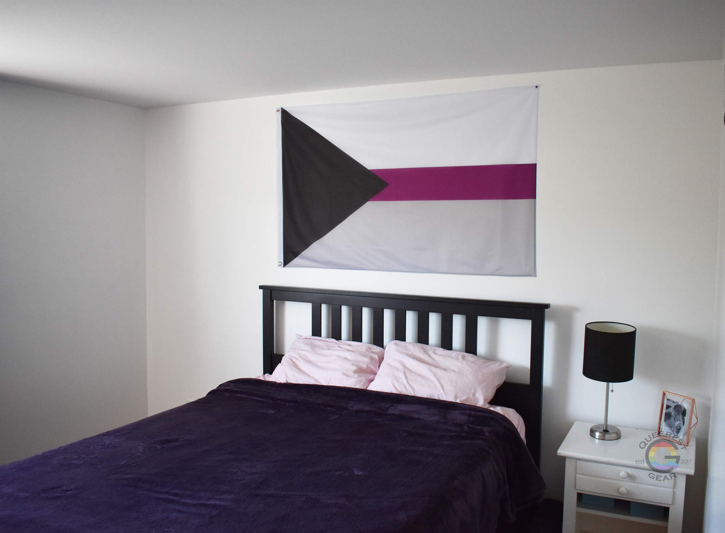3’x5’ demisexual pride flag hanging horizontally on the wall of a bedroom centered above a bed with a purple blanket