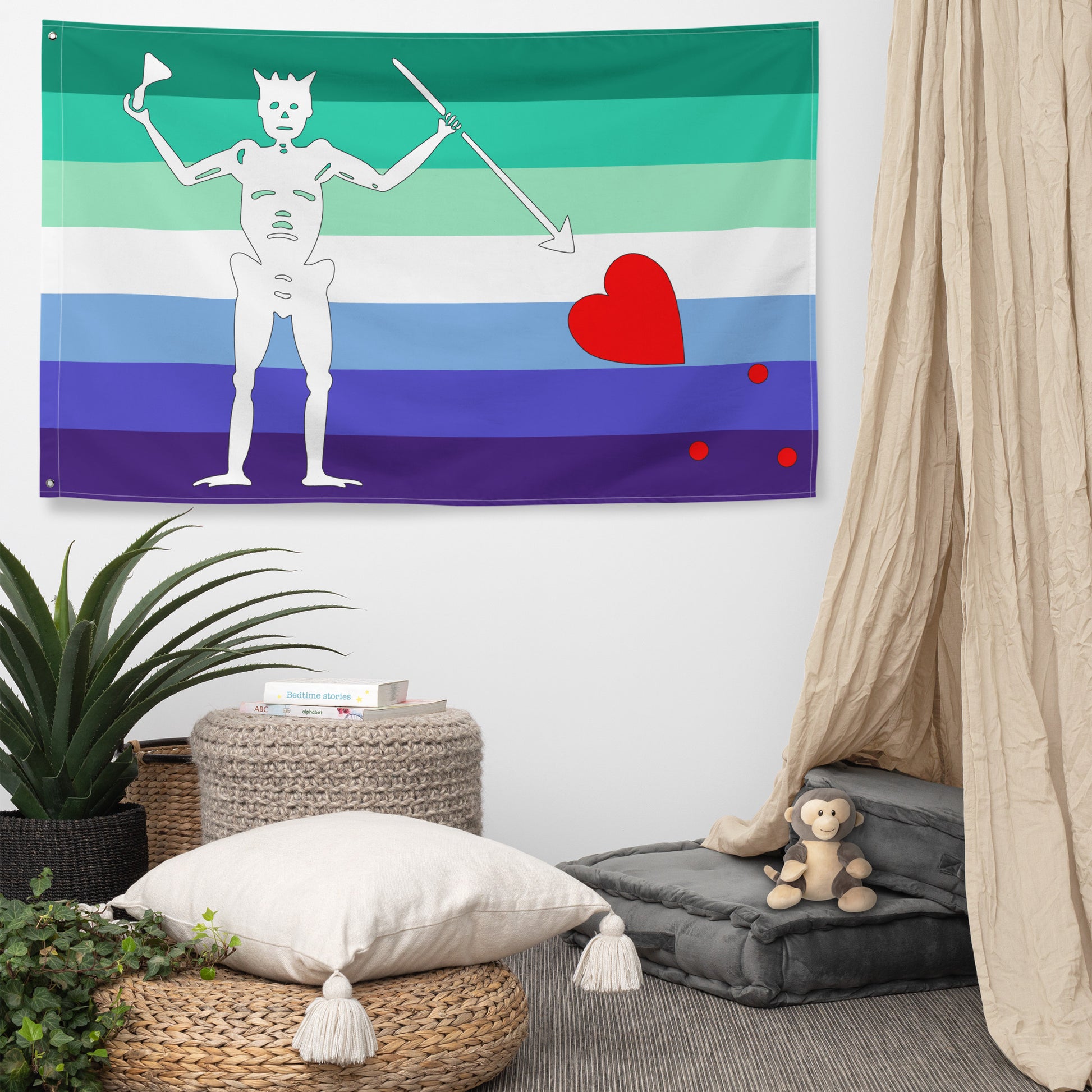 gay mlm blackbeard flag hanging on a white wall next to a curtain and above some cushions, an ottoman, and plants