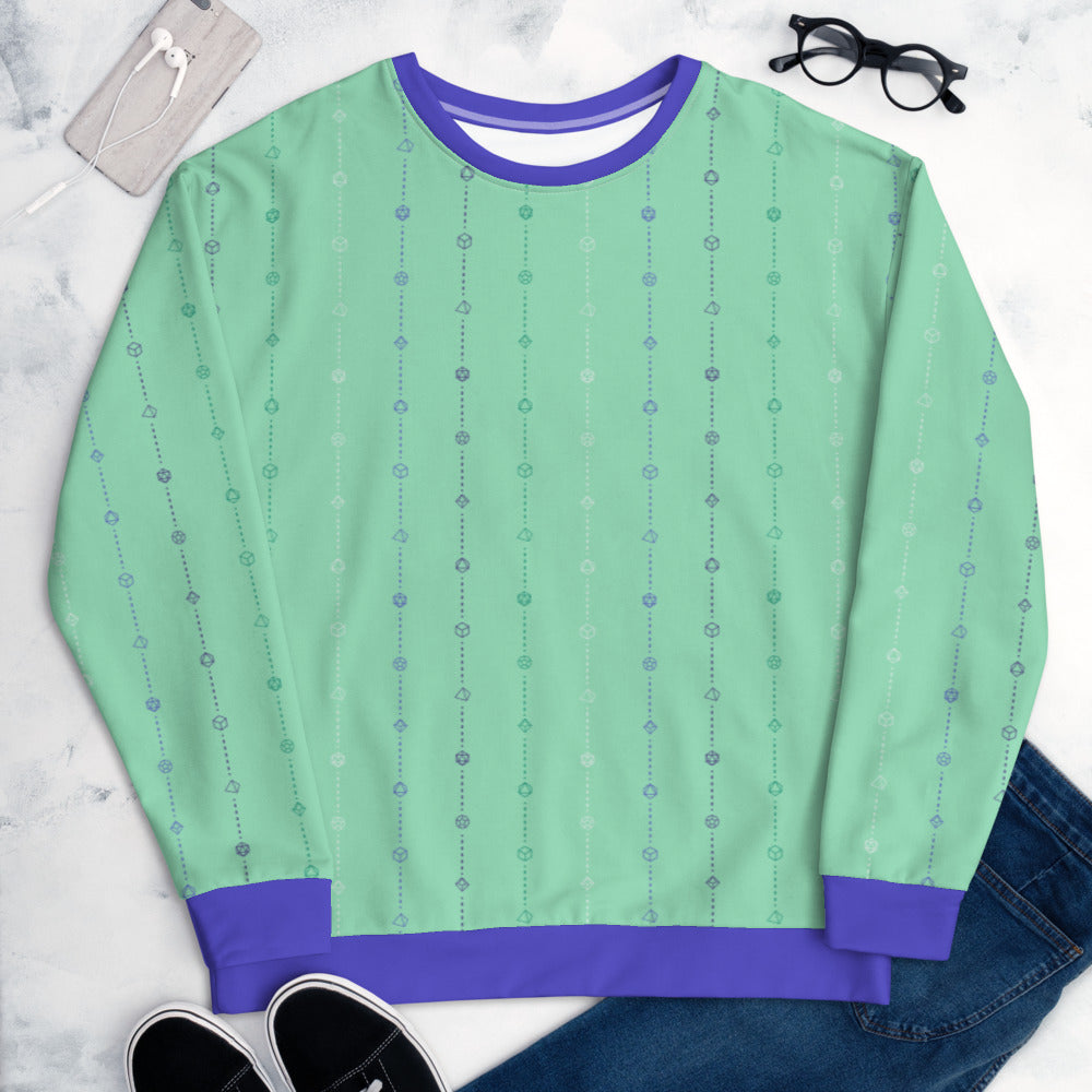 The gay mlm pride sweater laying flat, surrounded by clothes, a phone, and glasses. the sweater is green and has stripes of dashed lines and polyhedral dnd dice in blues, green, and white. The cuffs, collar, and waistband are a matching blue