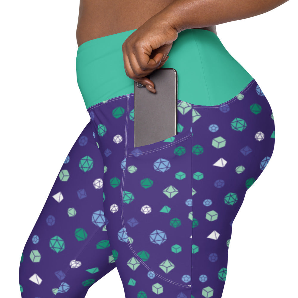left side view of gay mlm dnd dice plus size leggings. the dark-skinned female-presenting model is sliding her phone into one of the side pockets