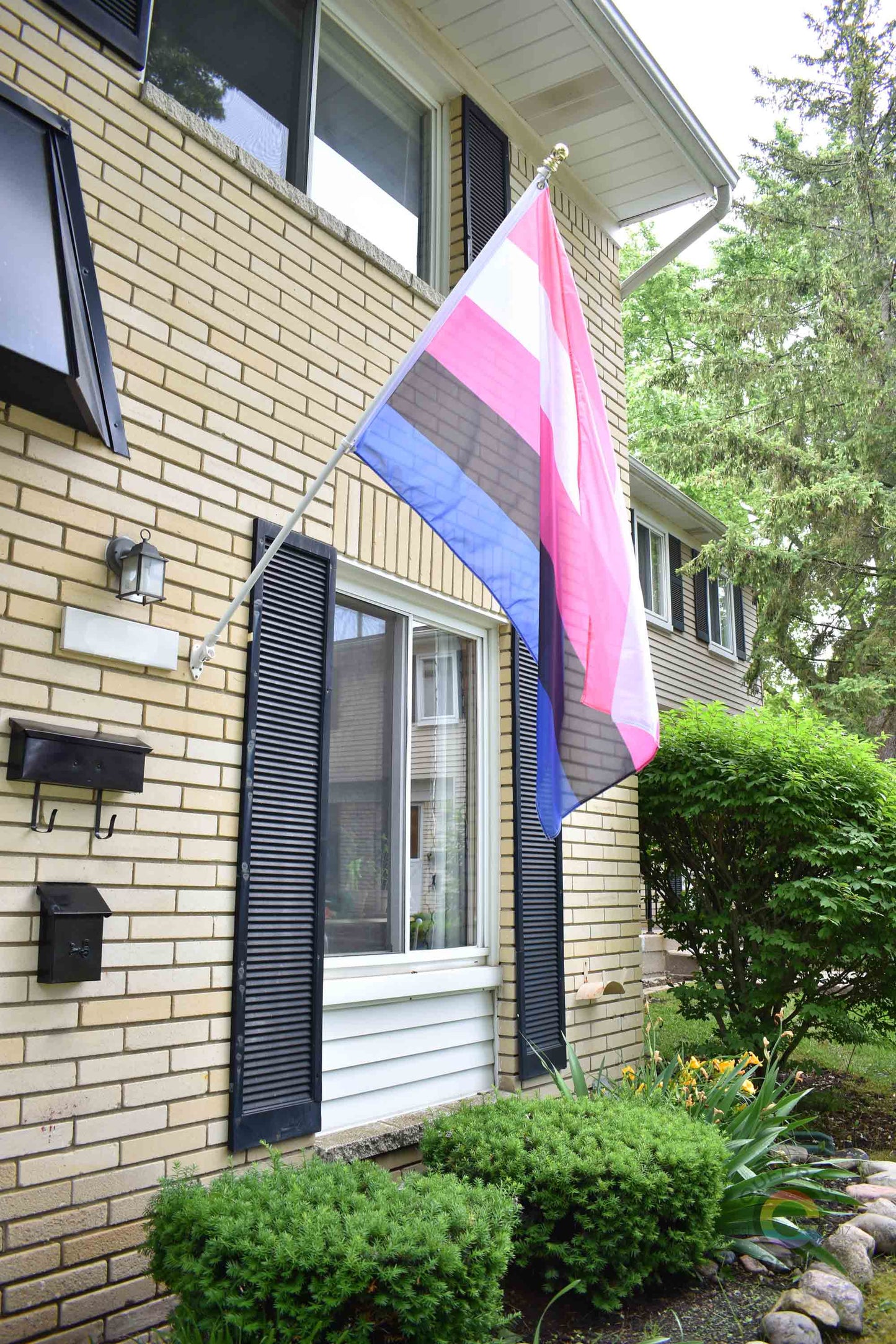 3’x5’ genderfluid pride flag hanging from a flagpole on the outside of a light brick house with dark shutters