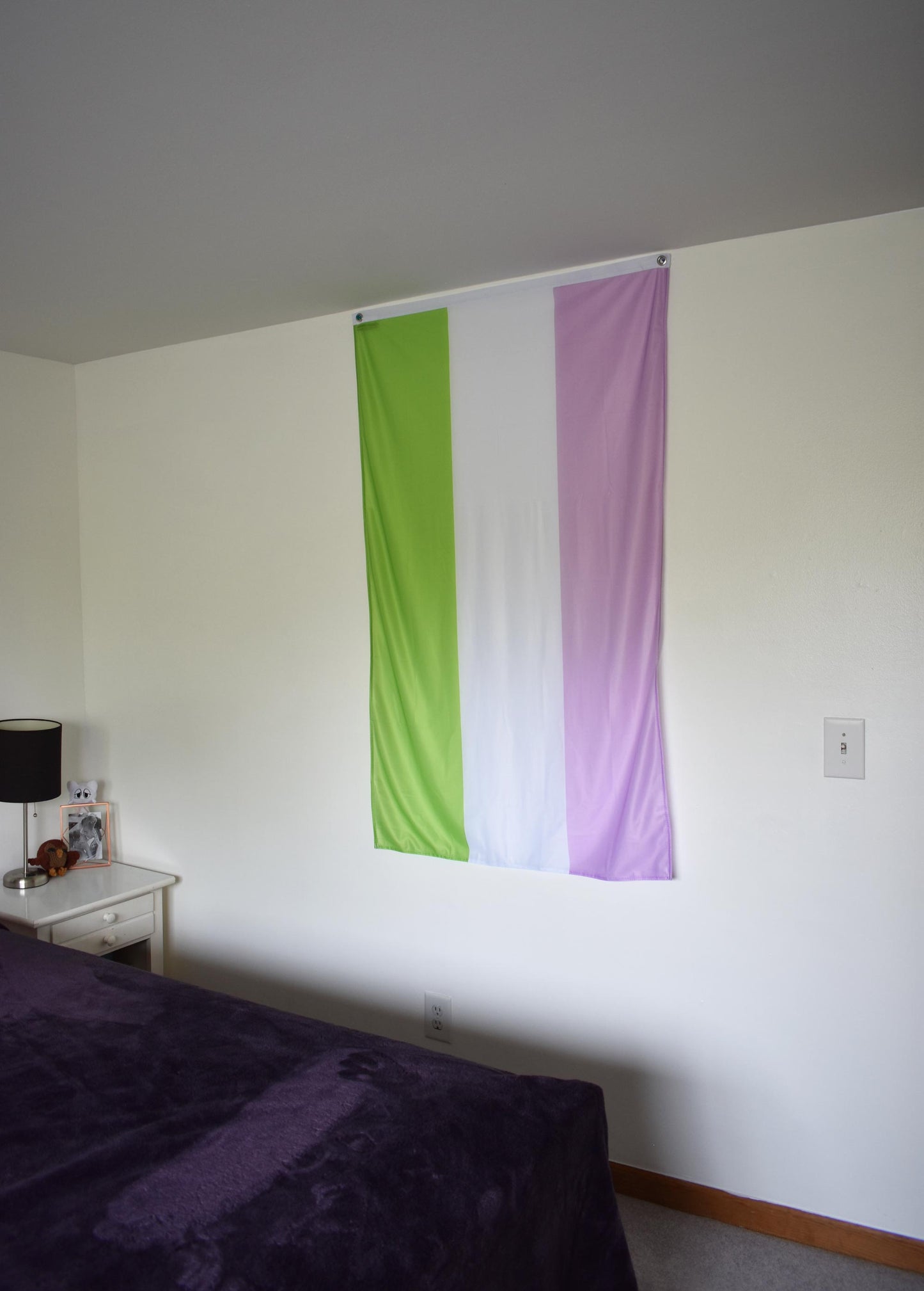 3’x5’ genderqueer flag hanging vertically on the wall of a bedroom with a nightstand and a bed