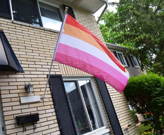 3’x5’ lesbian pride flag hanging from a flagpole on the outside of a light brick house with dark shutters