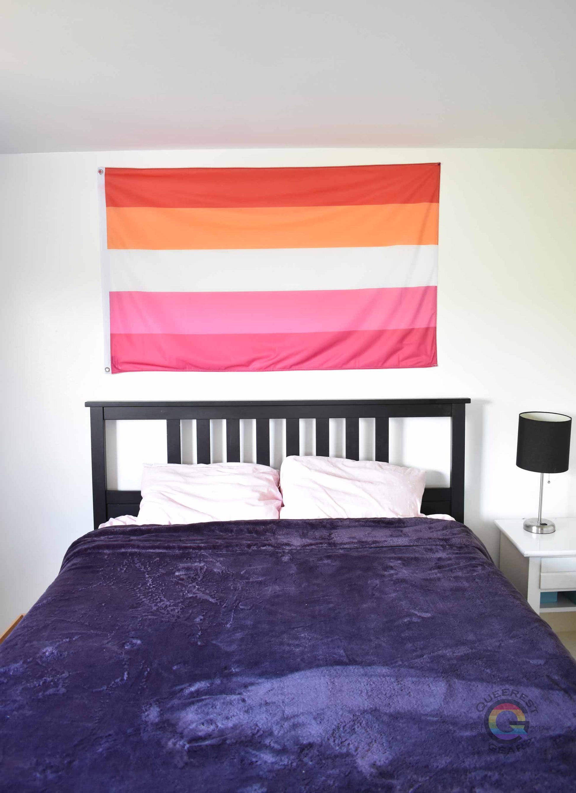 3’x5’ lesbian pride flag hanging horizontally on the wall of a bedroom centered above a bed with a purple blanket