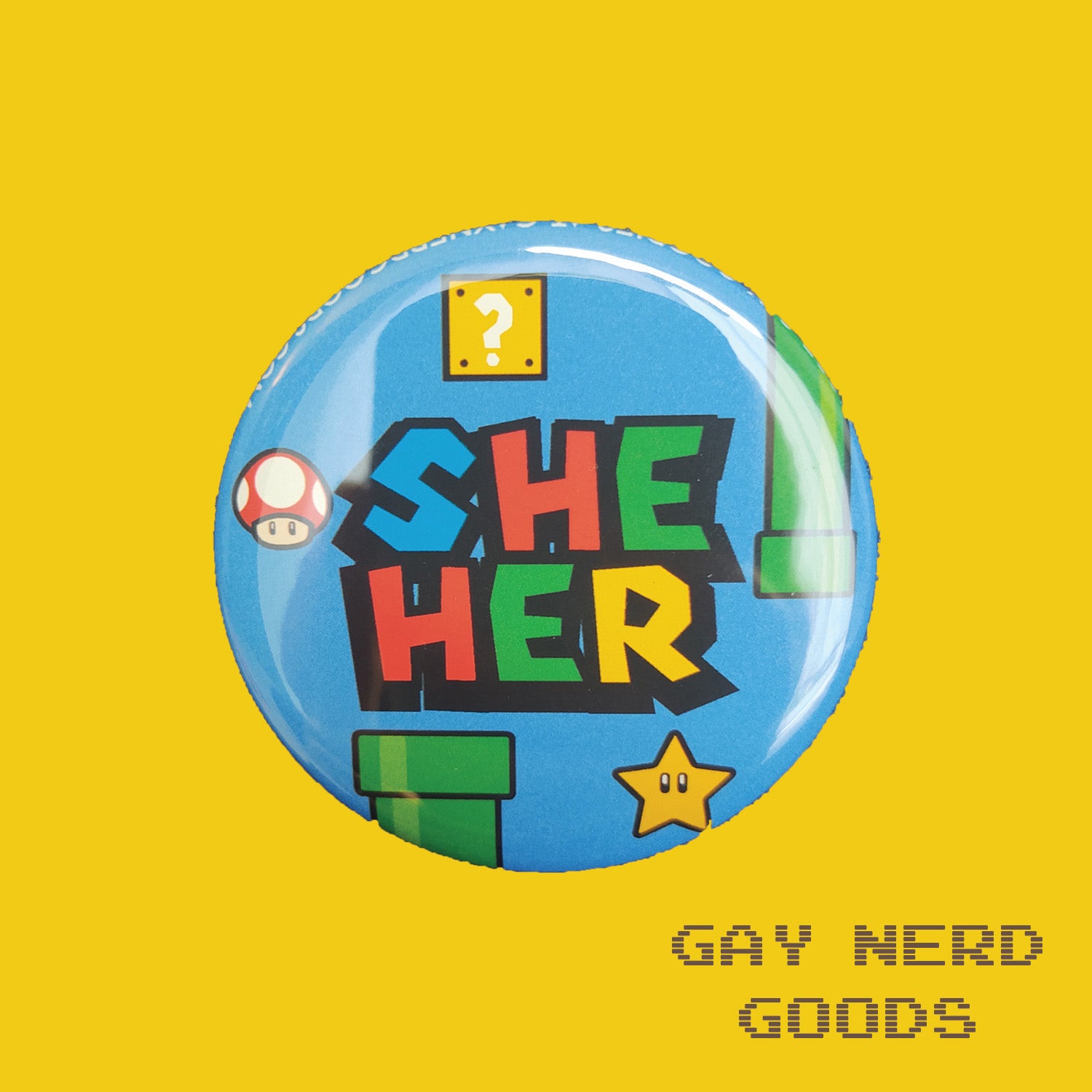 she her mario pronoun button with blue background, green pipes, question block, star, and mushroom on a yellow background