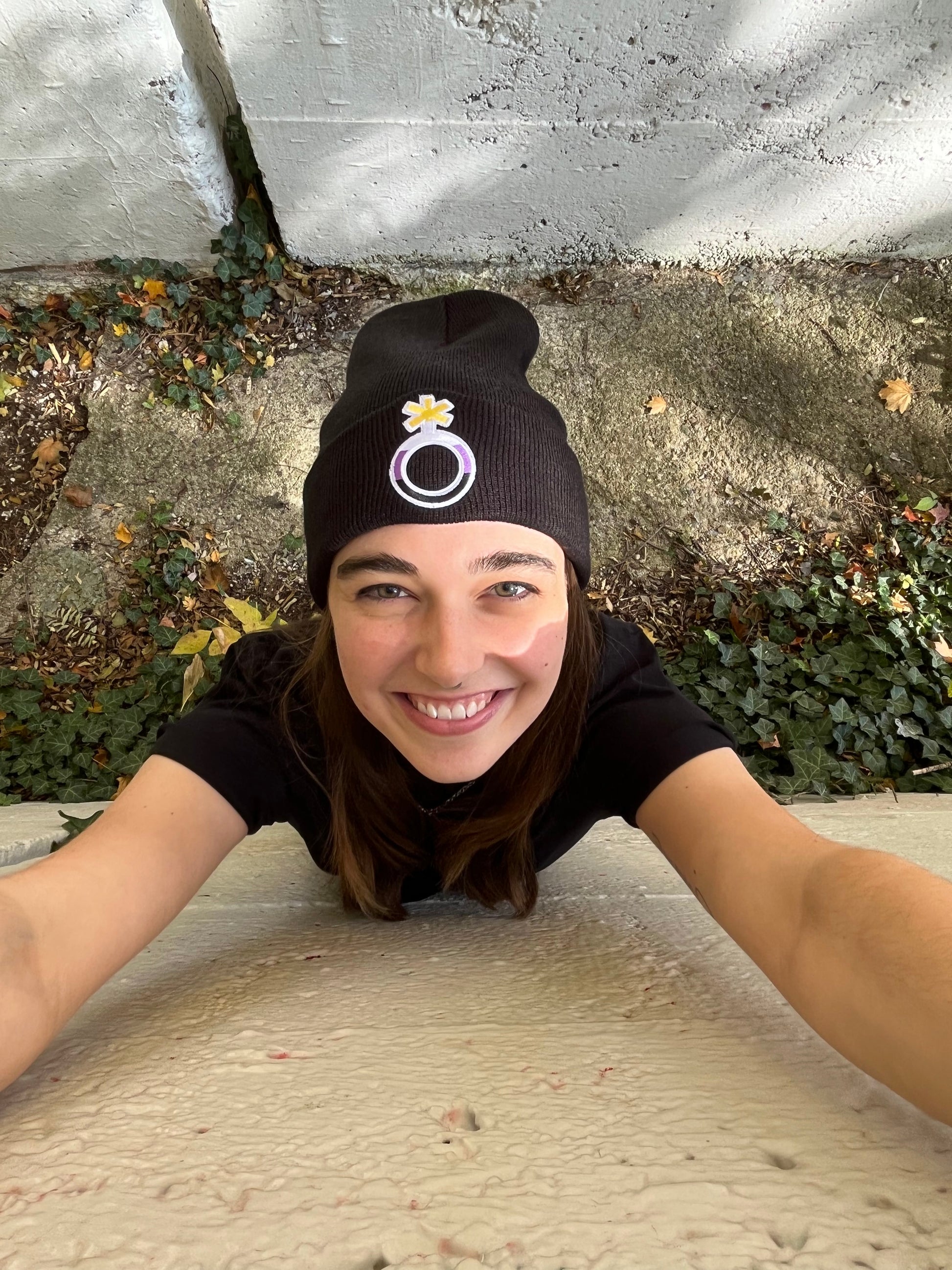 high angle looking down of person reaching up and smiling wearing the nonbinary pride beanie