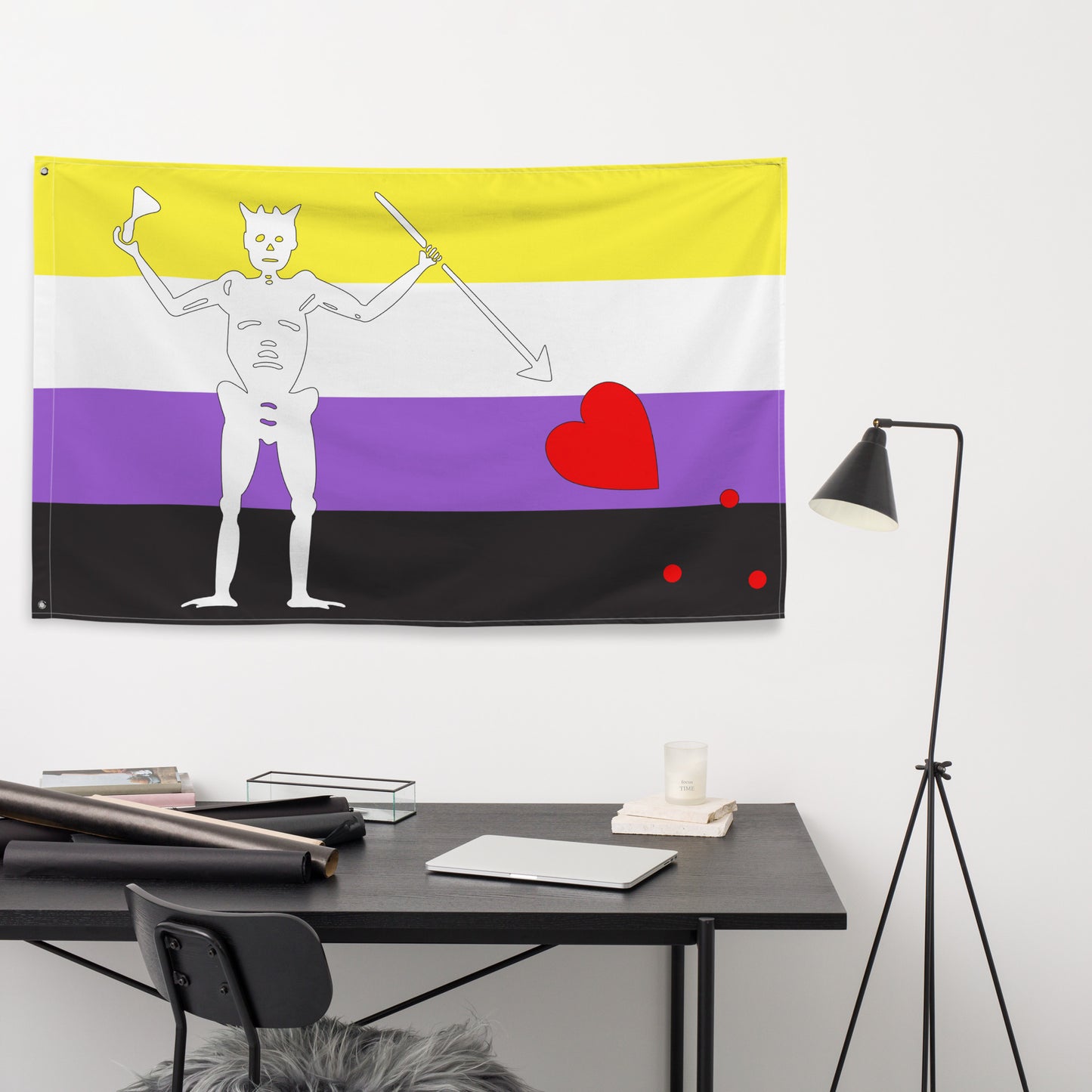 the nonbinary blackbeard pirate flag hanging on a white wall above a small black desk and lamp
