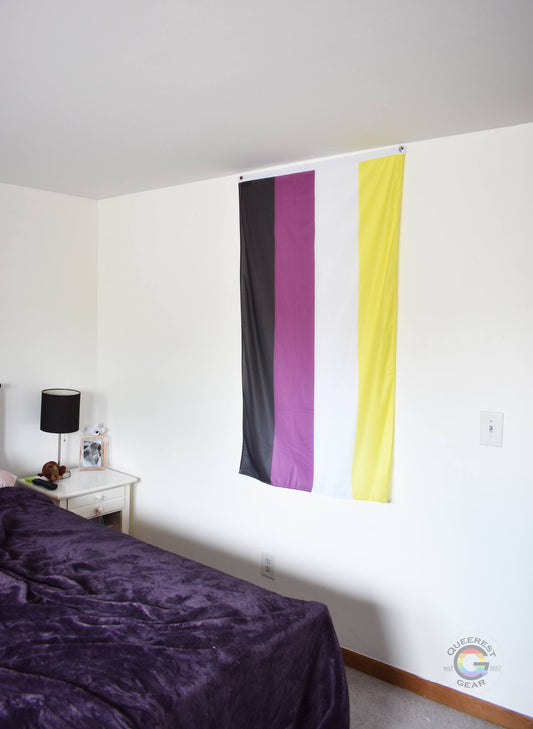  3’x5’ nonbinary flag hanging vertically on the wall of a bedroom with a nightstand and a bed