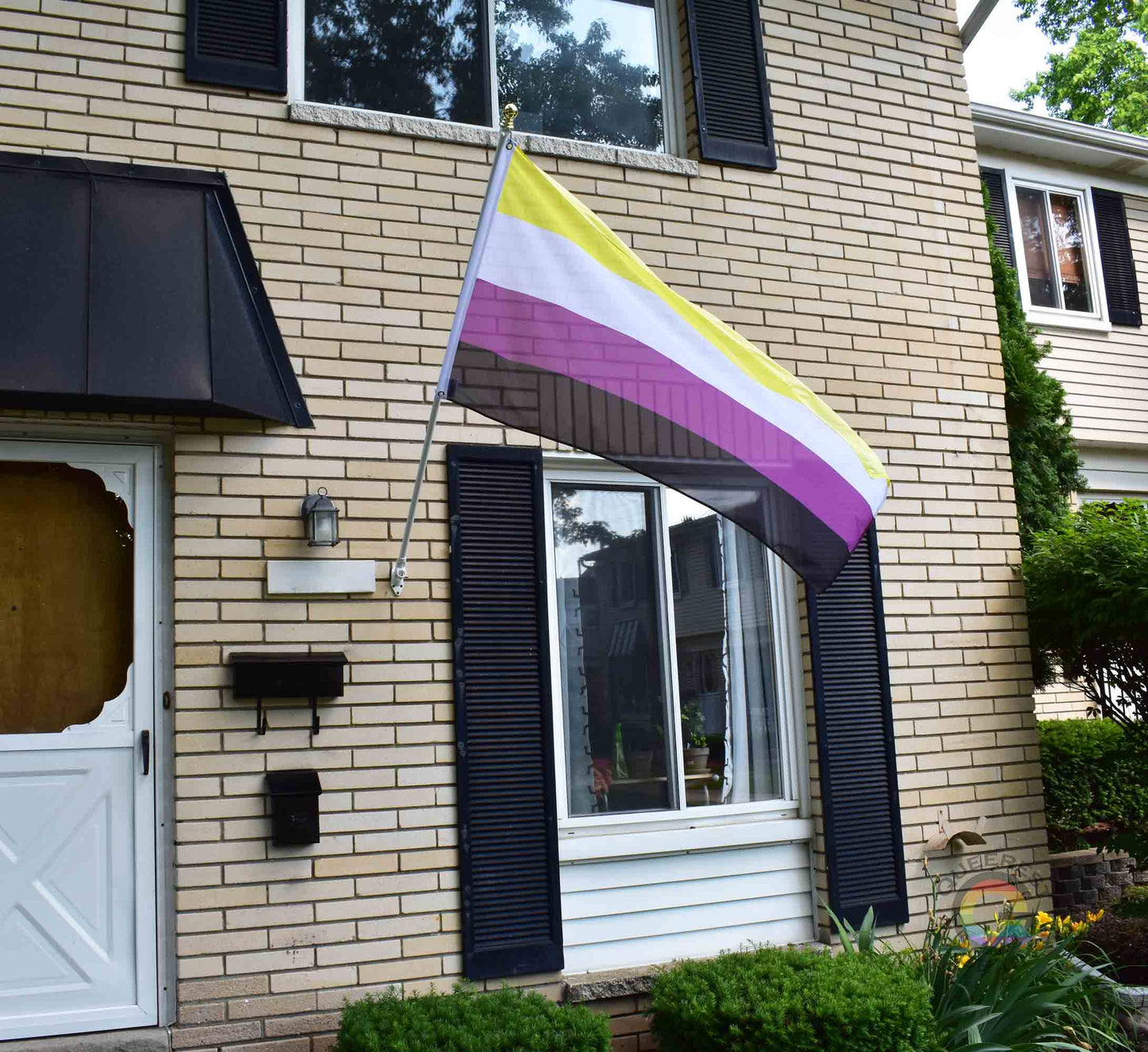 3’x5’ nonbinary pride flag hanging from a flagpole on the outside of a light brick house with dark shutters