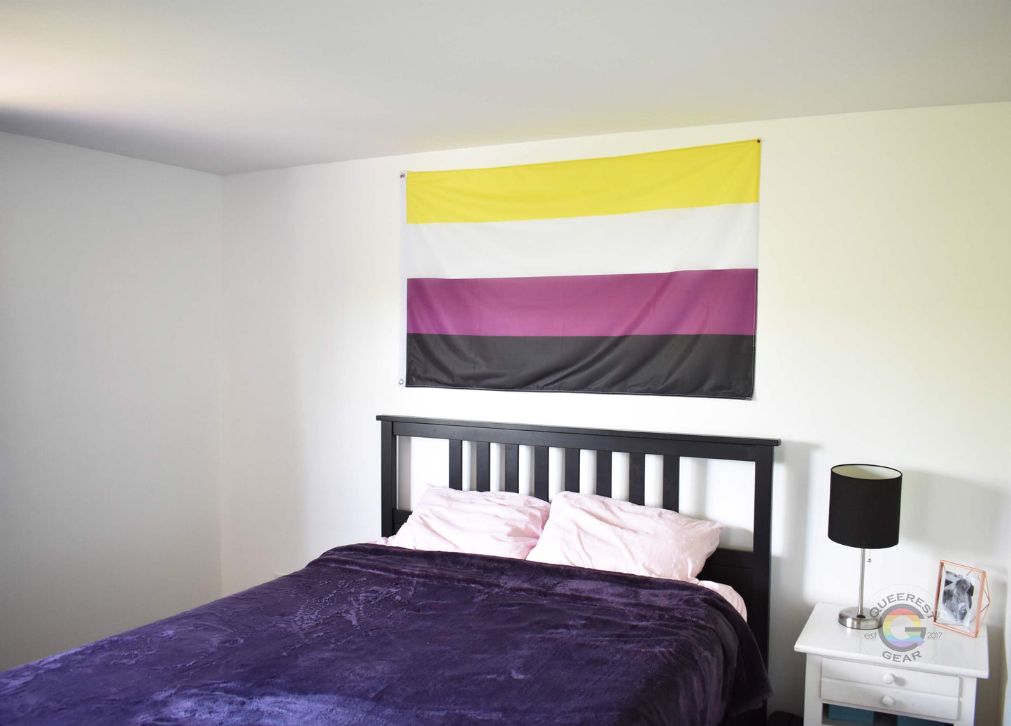 3’x5’ nonbinary pride flag hanging horizontally on the wall of a bedroom centered above a bed with a purple blanket