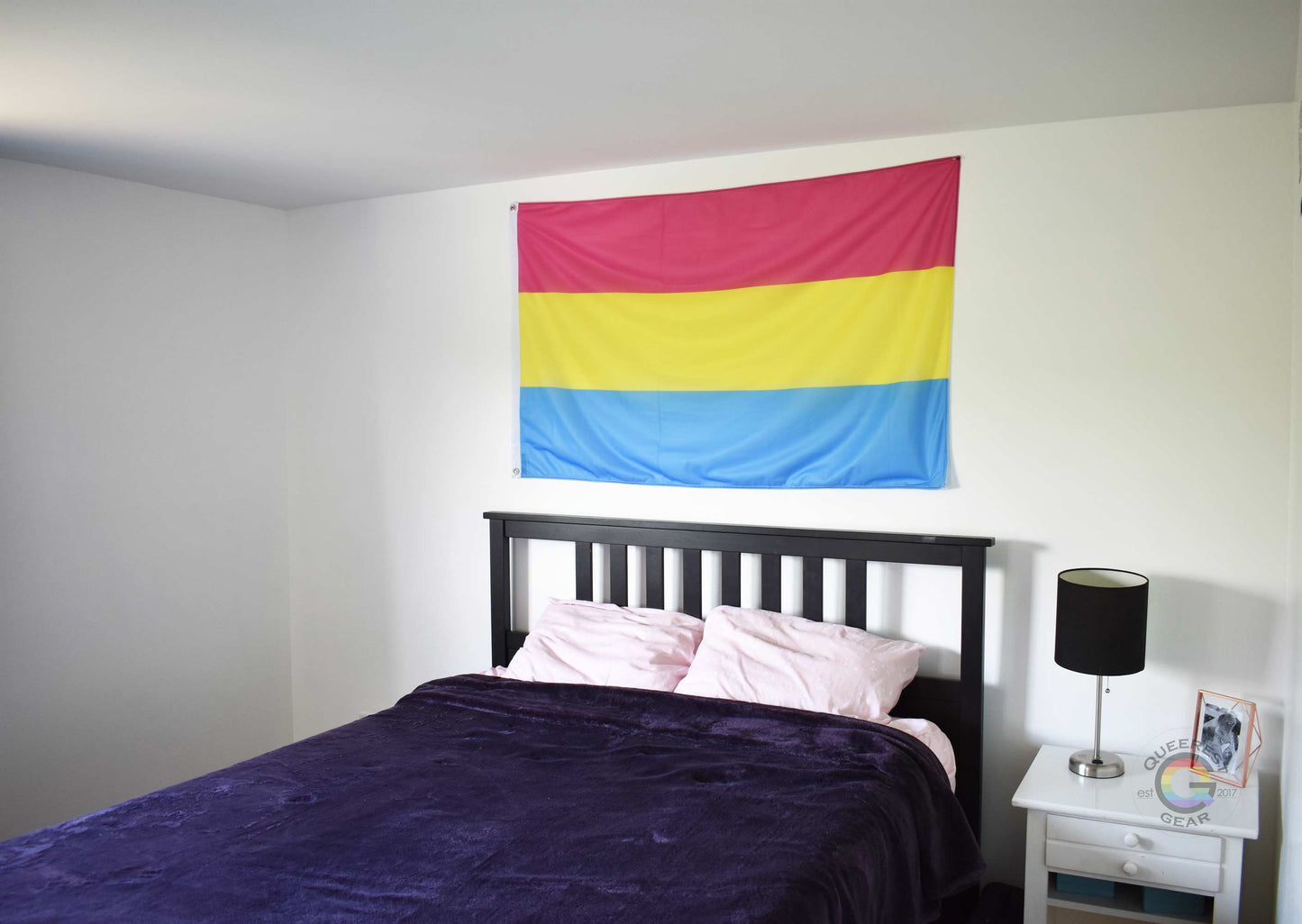 3’x5’ pansexual pride flag hanging horizontally on the wall of a bedroom centered above a bed with a purple blanket