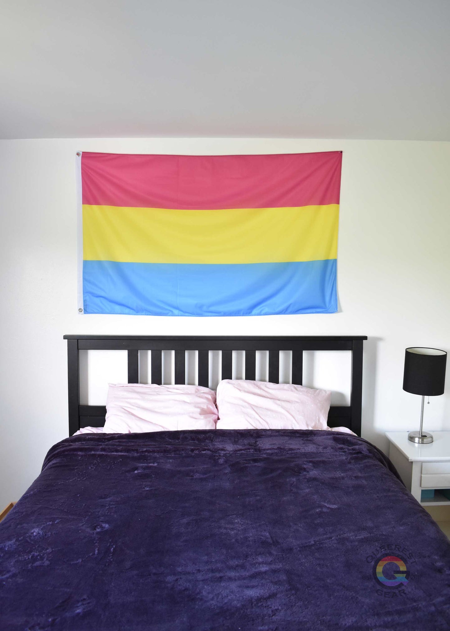 3’x5’ pansexual pride flag hanging horizontally on the wall of a bedroom centered above a bed with a purple blanket