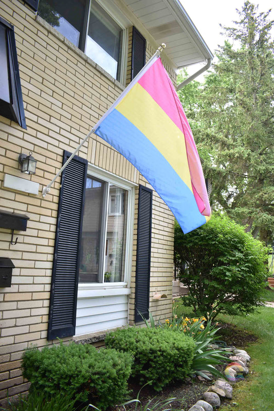  3’x5’ pansexual pride flag hanging from a flagpole on the outside of a light brick house with dark shutters