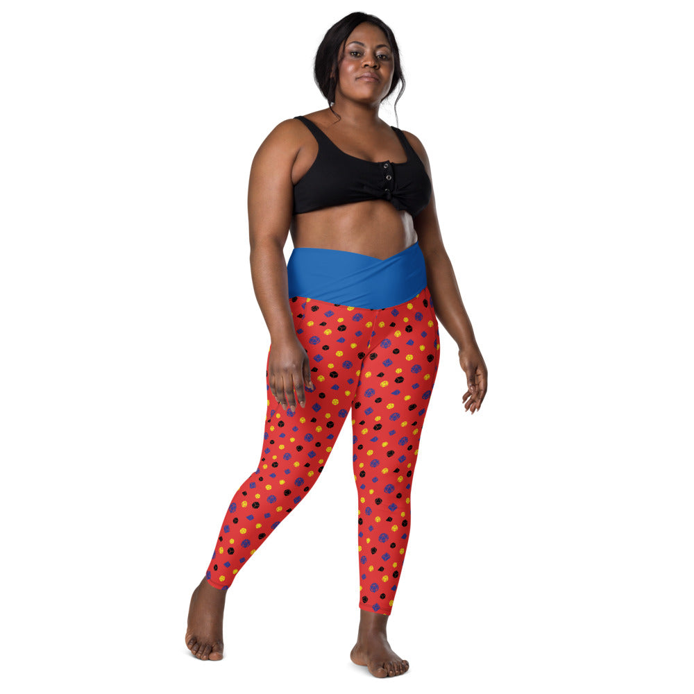front view of dark-skinned female-presenting plus size model wearing polyamory dice leggings and a black sports bra. This view shows off the blue crossover high-rise waistband
