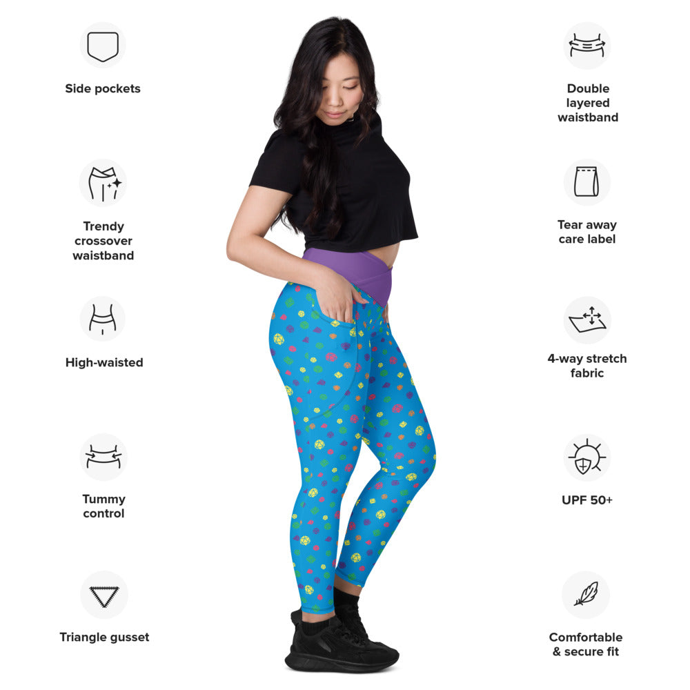 Light-skinned dark-haired female-presenting model wearing rainbow dice leggings. she is facing right and has a hand in the pocket. she is surrounded by product specs: "side pockets, trendy crossover waistband, high-waisted, tummy control, triangle gusset, double layered waistband, tear away care label, 4-way stretch fabric, UPF 50+, comfortable & secure fit