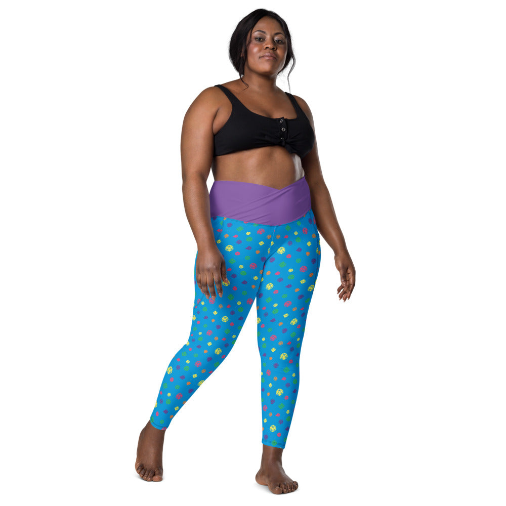 front view of dark-skinned female-presenting plus size model wearing rainbow dice leggings and a black sports bra. This view shows off the purple crossover high-rise waistband