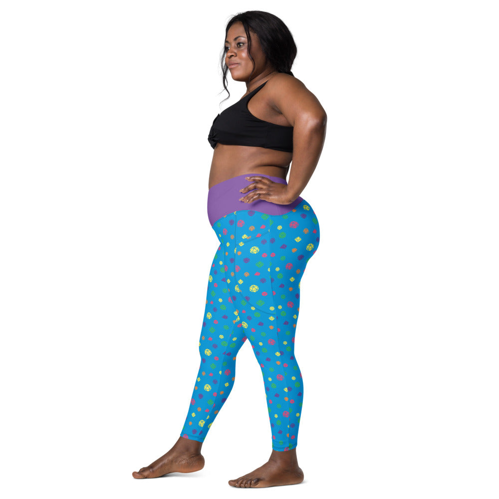 Left side view of dark-skinned female-presenting model wearing the rainbow dice leggings and black sports bra. She is facing left with her left hand on her hip and right leg forward