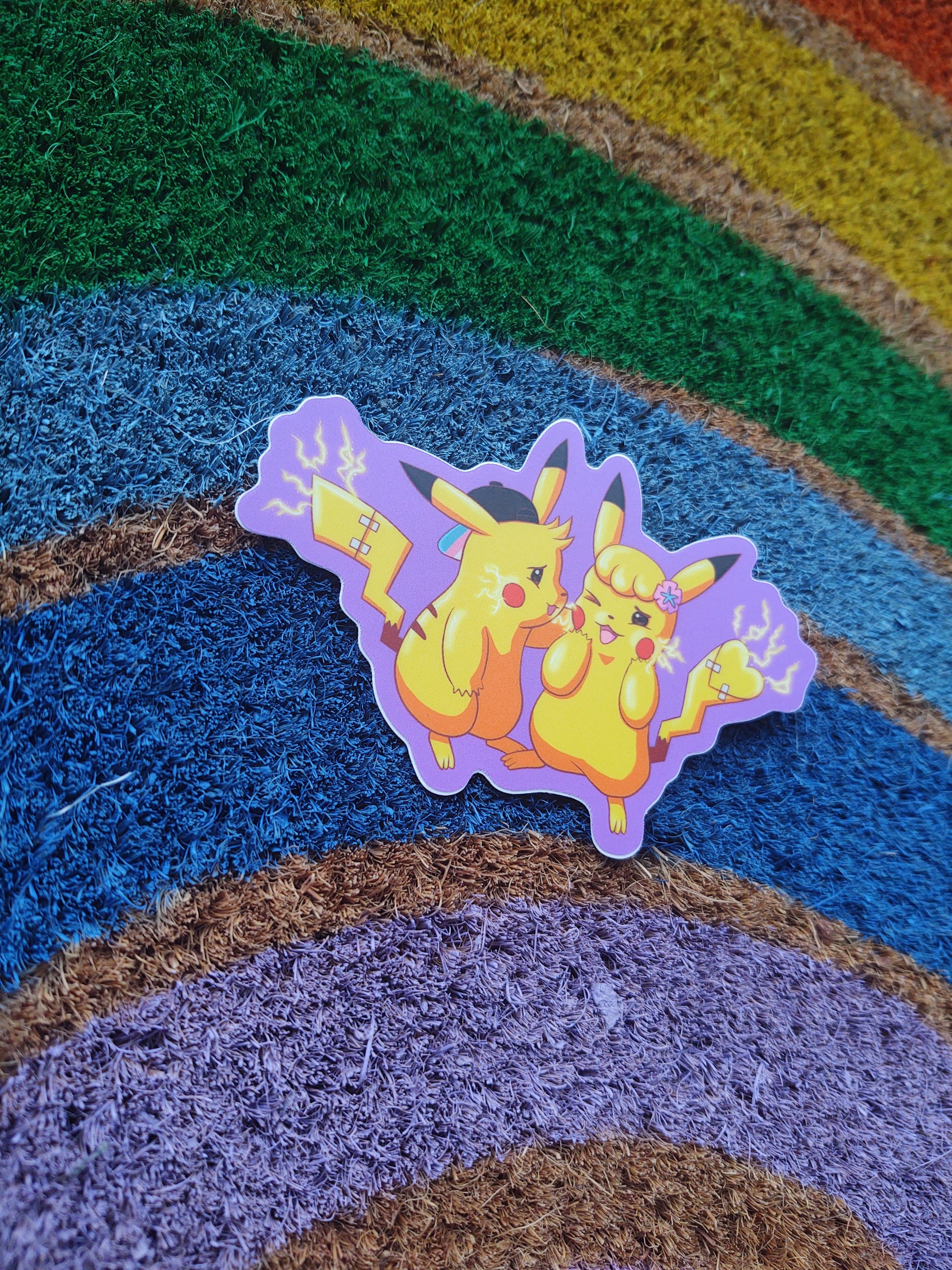 the trans for trans sticker at an angle on a rough rainbow background. the sticker is a pair of transgender animals with electric current flowing and a purple outline