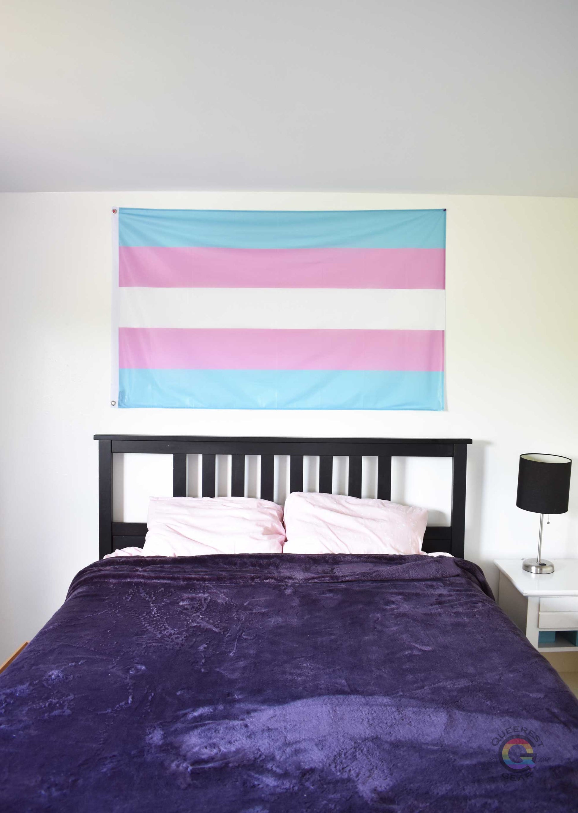 3’x5’ transgender pride flag hanging horizontally on the wall of a bedroom centered above a bed with a purple blanket